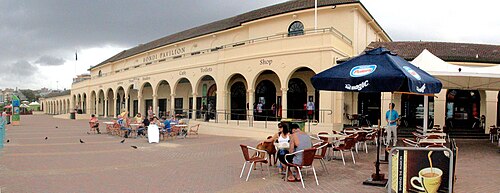 The Bondi Pavilion's ground floor arches along the promenade, cafe tables and blue umbrellas set out underneath them.