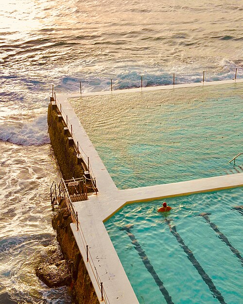 The Icebergs pool cut into the rocks at the southern end, turquoise water inside a white concrete surround with the ocean breaking over the far wall.