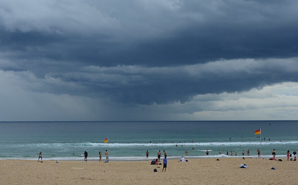 Swimmers gathered near the yellow and red patrol flags on the sand as a storm front moves out over the water.