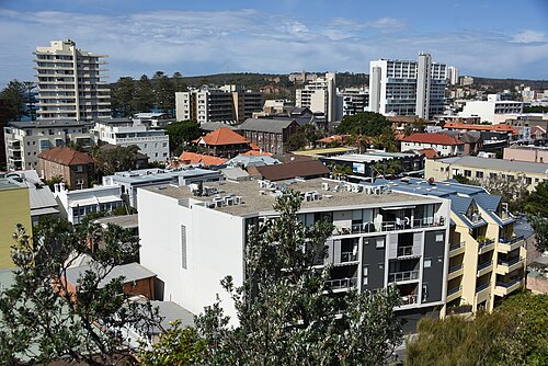 An elevated view over low rise rooftops and apartment buildings with green foliage between them.