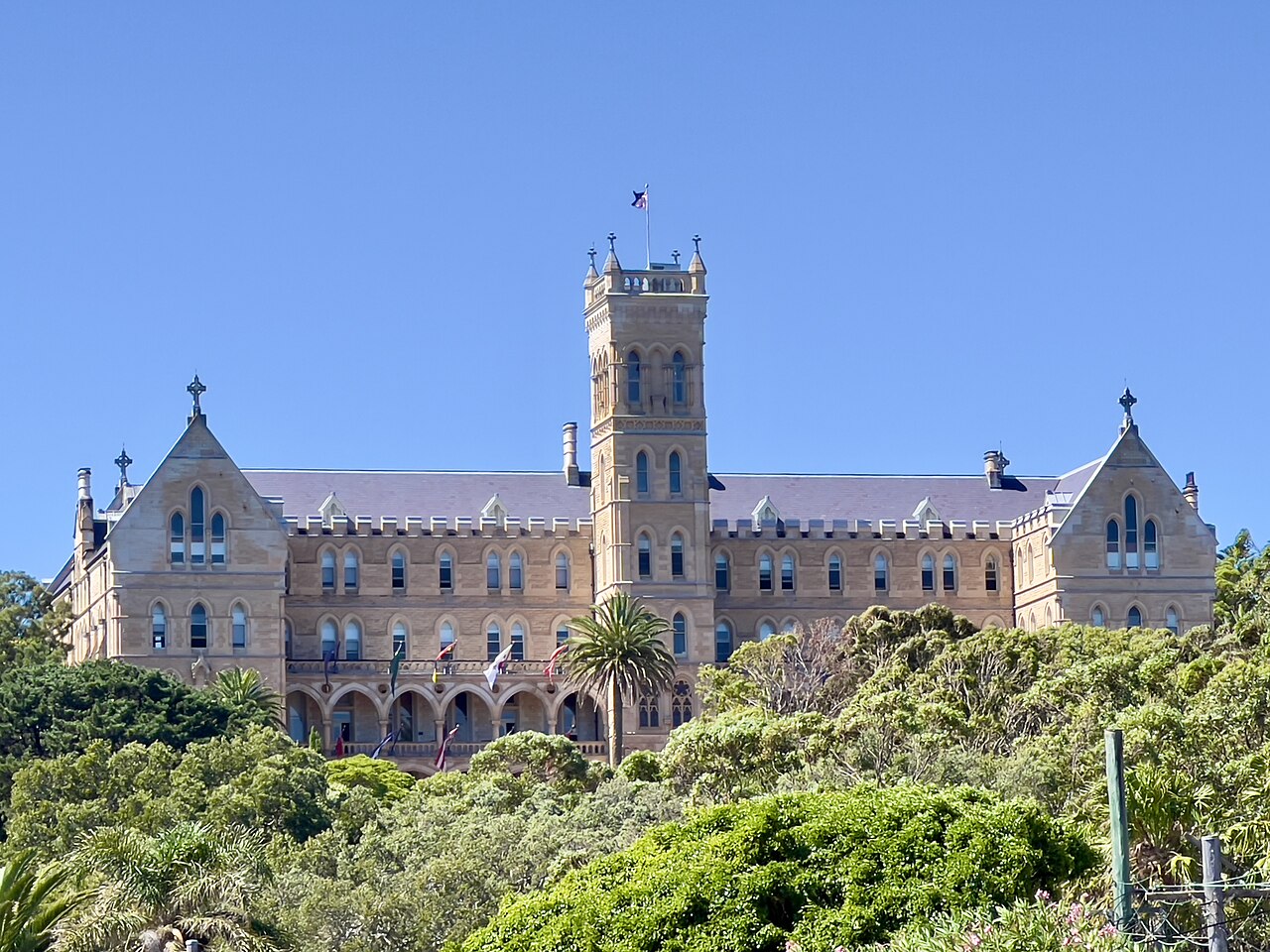 A sandstone Gothic building with a tall central tower rising above the trees on the seminary's grounds.
