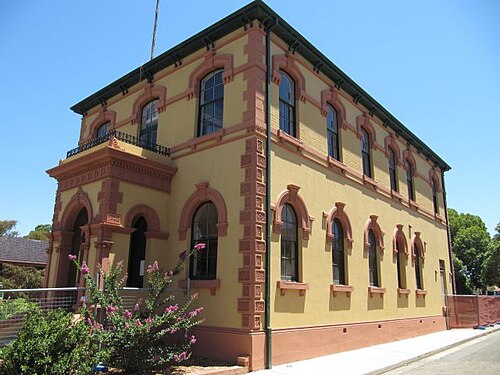 The former Marrickville Town Hall on Illawarra Road, a two storey rendered corner building with arched window heads, a bracketed cornice and a first floor balustraded balcony.