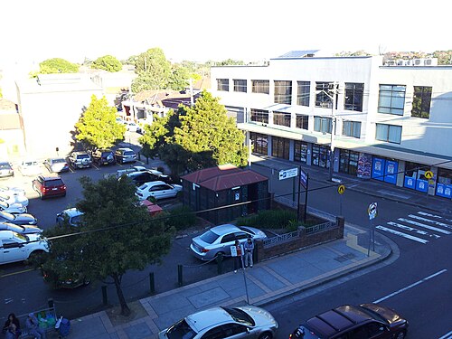 An elevated view of a rear car park beside Illawarra Road, a brick amenities block, parked cars and multi storey commercial buildings behind.