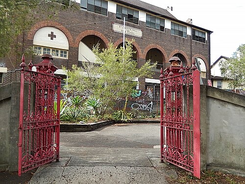 The wrought iron gates of St Joseph's Boys School opening onto an arched brick cloister building lettered ST JOSEPH'S HALL above.