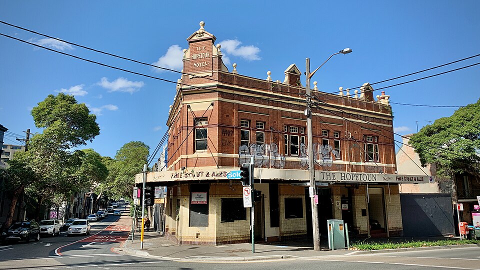 The Hopetoun Hotel's corner tower and parapet at Bourke and Fitzroy Streets, ground floor windows shuttered and taped over, graffiti tags across the upper storey.