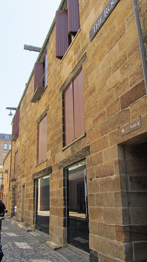 A sandstone warehouse wall along Kendall Lane, tall window openings closed with timber shutters under a plain parapet.