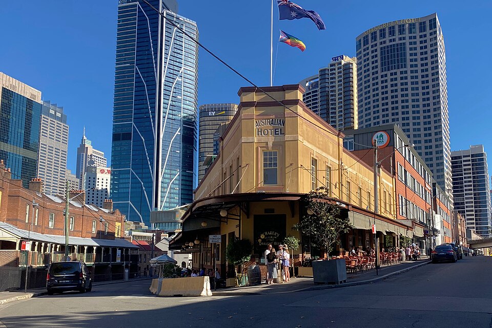The Australian Hotel's rendered corner building on Cumberland Street, glass office towers rising directly behind its parapet and flagpoles.