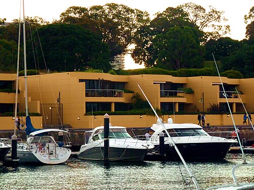 Yachts and motor cruisers moored at the wharf's marina in front of a curved row of harbourside apartments.