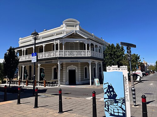 The Dockside Tavern on the corner at McLaren Parade, two storeys with cast iron lace along the upstairs balcony, tables and folded umbrellas out on the paving.