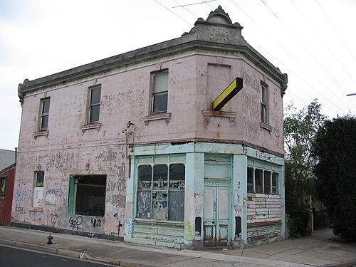 Clifton House on the corner of Edward and Ewing Streets, a two storey corner building in pink and pale blue render with 1890 worked into its pediment.