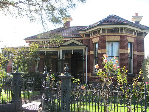A single storey brick Victorian villa with decorative porch ironwork behind an ornate wrought iron front fence.
