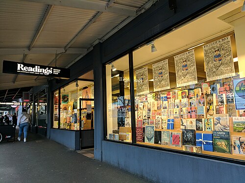 The footpath under Readings bookshop's wide metal verandah on Lygon Street, large window displays and black overhead signage.