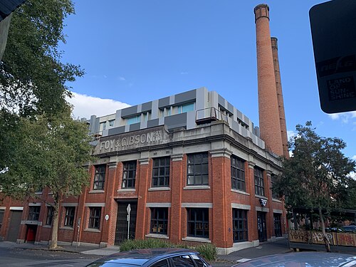 The former Foy & Gibson warehouse on Stanley Street, red brick with concrete trim, large metal framed windows and brick chimneys, the FOY AND GIBSON PTY LTD lettering still on the wall.