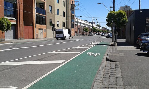 Wellington Street, bluestone gutters and a protected bike lane running past multi storey brick buildings.