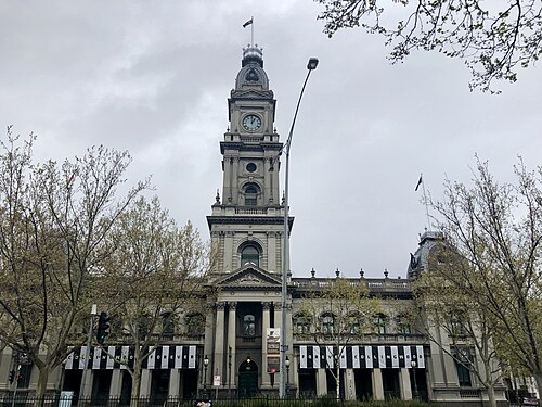 The Collingwood Town Hall's clock tower and columned front, rendered masonry with a banner strung across it.