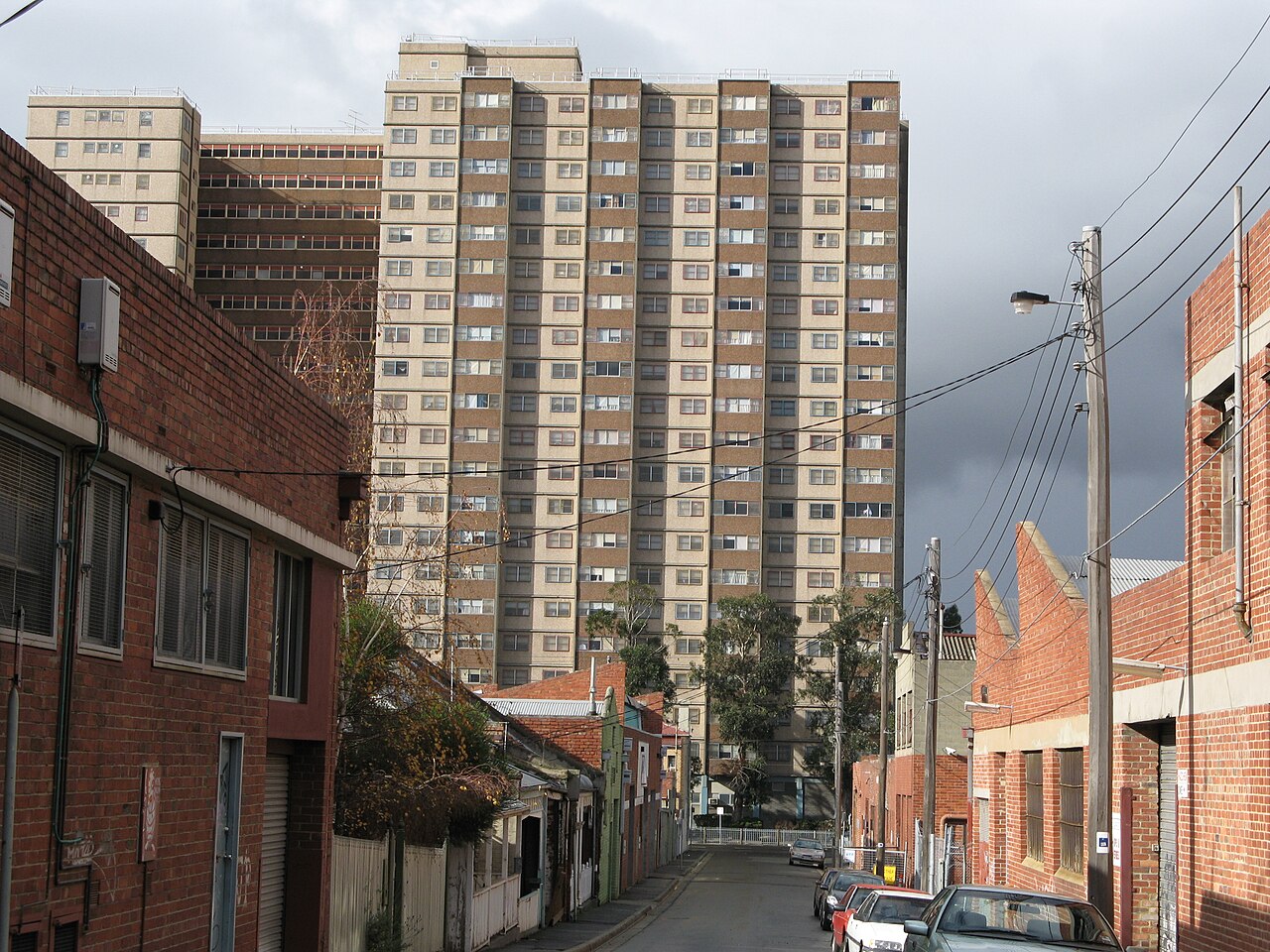 A narrow lane between red brick industrial and residential buildings, leading toward one of Collingwood's high rise Housing Commission towers.