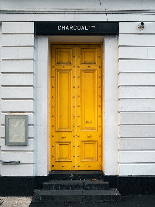 Yellow double doors set into a white rusticated masonry facade on Gertrude Street, the Charcoal Lane sign beside the doorway.