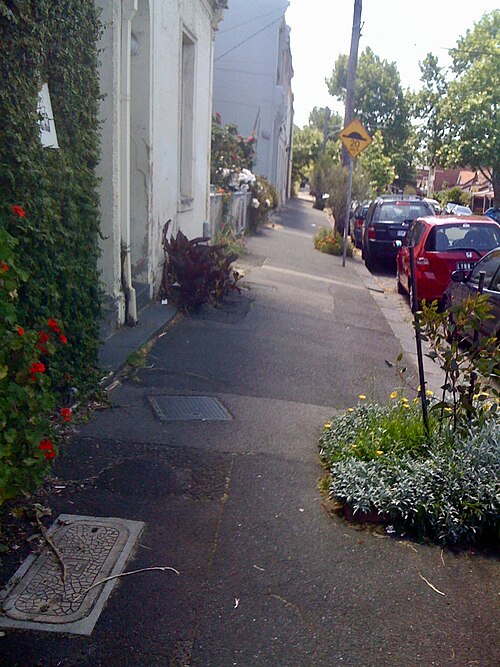 An ivy covered wall and small front gardens along the Gore Street footpath, parked cars at the kerb.
