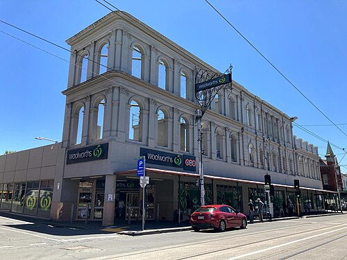 A three storey heritage facade with arched upper windows on Smith Street, a Woolworths sign filling the ground floor storefront.