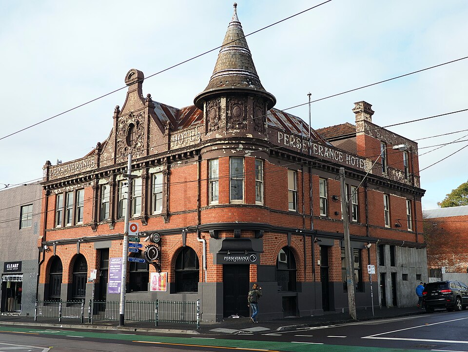 A two storey brick corner pub with a corner turret and decorative parapet over the ground floor bar, Perseverance Hotel signage above the door.