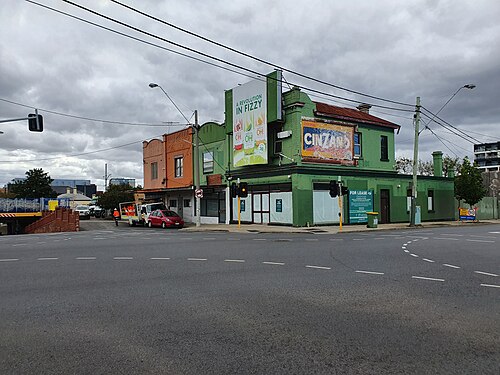 A two storey green brick commercial building on the corner of Buckley and Victoria Streets, advertising billboards on its upper wall.