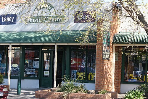 A single storey Byron Street shopfront with a green corrugated metal awning and a brick pillar planter box.