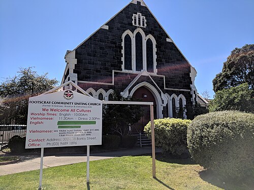 A dark bluestone church with pointed gothic arches and a steep gabled roof behind a low front lawn.