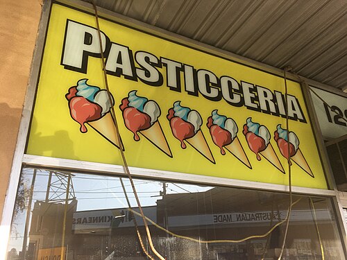 A yellow backlit Pasticceria shop sign with ice cream cone illustrations above a glass shopfront window.
