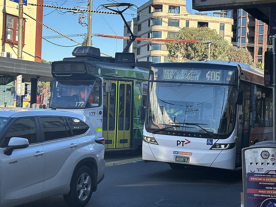 A tram and a bus stopped at the Footscray Station interchange on Irving Street, modern apartment towers behind.