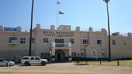 The Royal Melbourne Yacht Squadron's beige rendered clubhouse with an arched entrance, palms and cars along its gravel driveway.