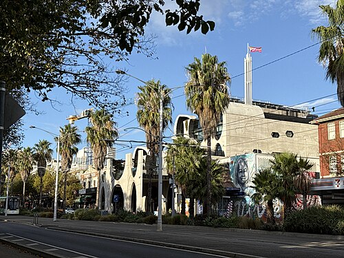 The Victorian Pride Centre's off form concrete arches on Fitzroy Street, palms in front and a mural on the wall beside it.