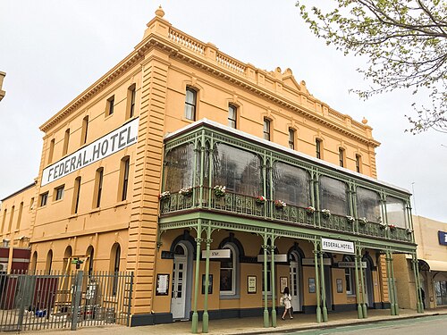 The Federal Hotel on William Street, three storeys of rendered brick with a green cast iron verandah across the front and its name painted along the side wall.