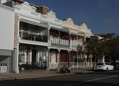 Four two storey terrace houses on Point Street in limestone and red brick, with white iron lace balconies and rendered parapets, one of them empty and up for lease.