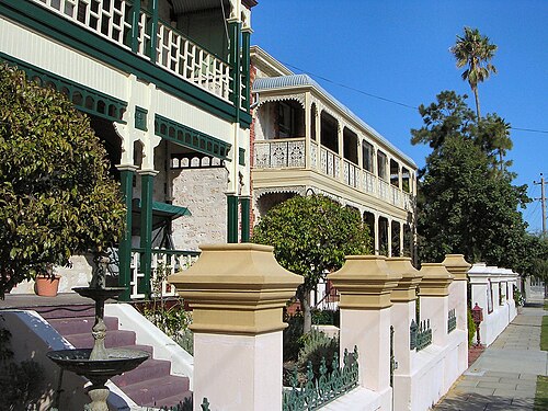 Two storey houses on Ord Street behind rendered gate piers and iron palisade fencing, with timber verandahs on both floors and a fountain in the front garden.