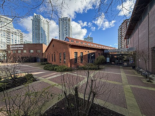 The old CPR roundhouse on Drake Street, a red brick building with a peaked skylight roof, glass towers rising behind it.
