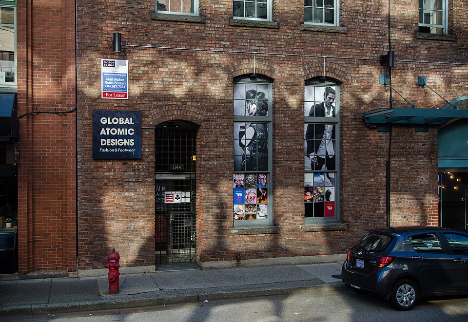 The ground floor of the Yaletown Building at 1152 Mainland Street, red brick with arched window heads, a storefront sign and a parked car on the street below.