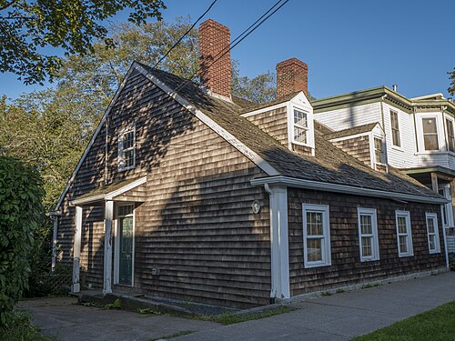 Akins House at 2151 Brunswick Street, a low shingled cottage with two brick chimneys and dormer windows, standing right on the sidewalk beside a taller shingled house.