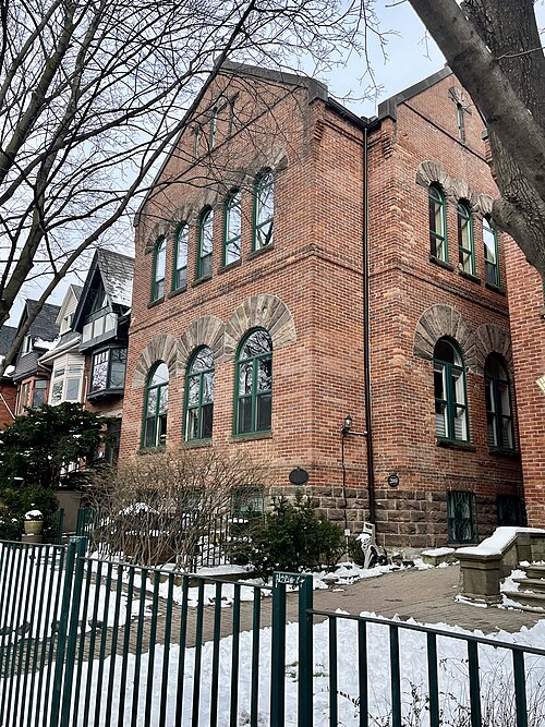 A red brick building on Sumach Street with round arched windows under carved stone hoods, seen from the corner in winter with snow on the ground.