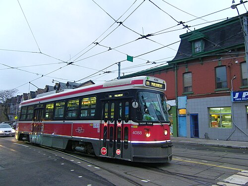A red and cream TTC streetcar on the 505 Parliament route stopped near Dundas and Parliament Streets, a red brick building with a green mansard roof behind it.