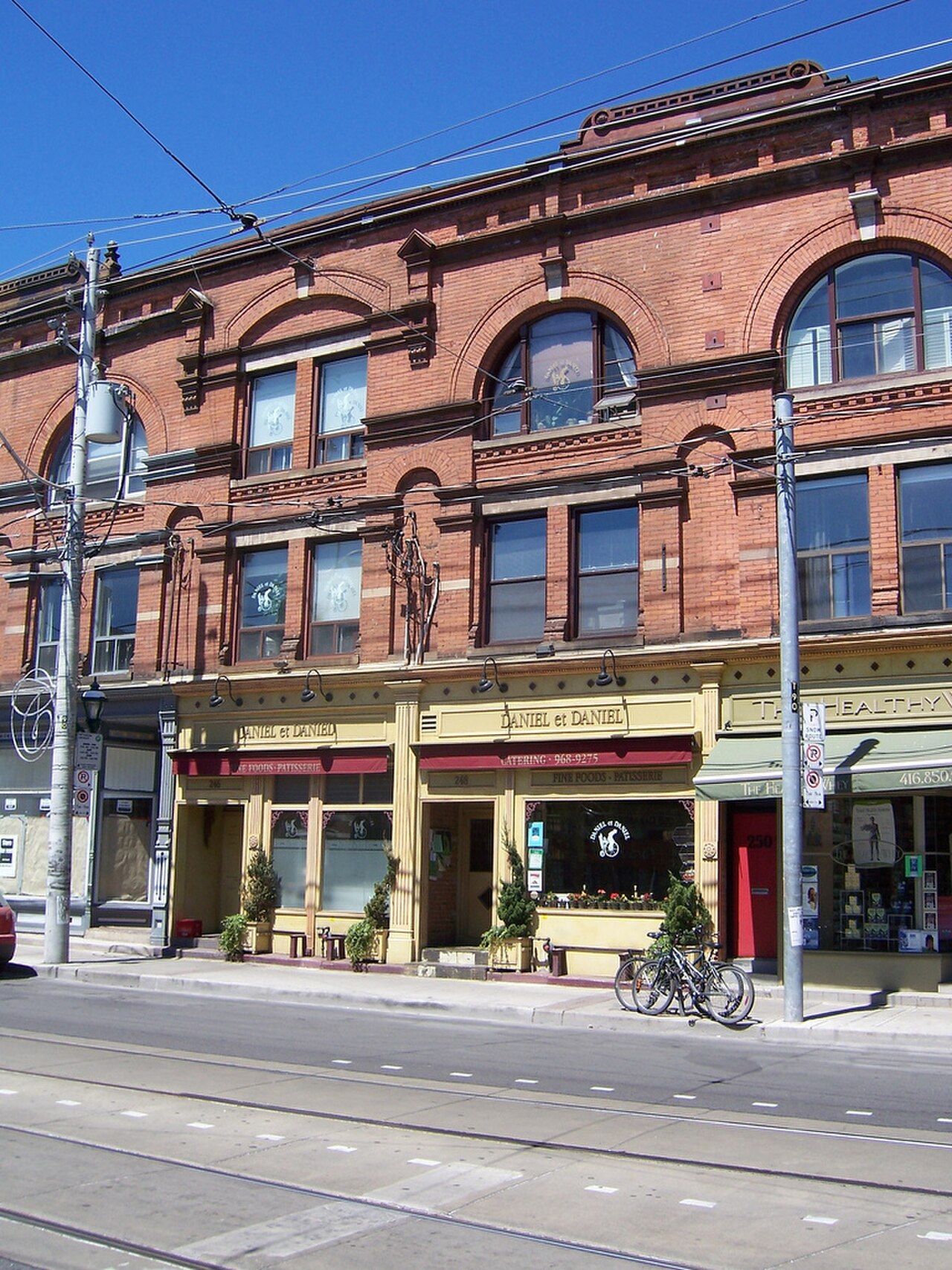 A red brick commercial building on Carlton Street with arched second floor windows, the Daniel et Daniel bakery storefronts at street level under striped awnings.