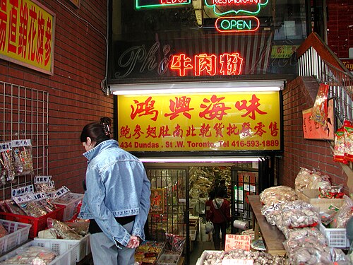 A woman looking over bins of dried, cellophane wrapped squid outside a shop at 434 Dundas Street West.