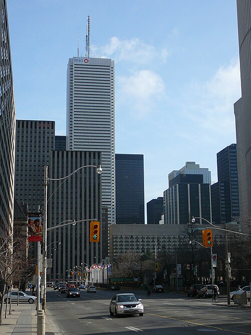 The white tower of First Canadian Place, marked BMO near its top, framed between two darker office towers, with a restaurant banner and a traffic light on the street below.