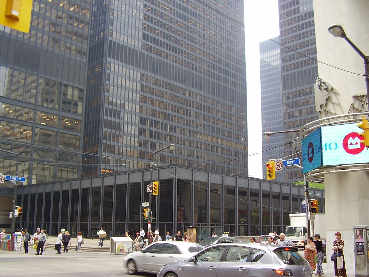 The intersection of King Street West and Bay Street, a Bank of Montreal sign on a curved corner building, dark glass office towers rising on both sides, and pedestrians crossing at the light.