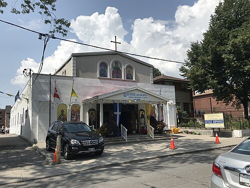 St. Irene Chrysovalantou Greek Orthodox Church on Gough Avenue, a white stucco facade with three icon medallions over the entrance and a cross at the peak.