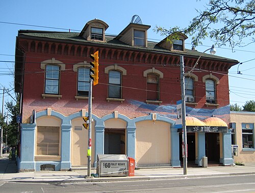 The Duke Hotel building at Leslie Street and Queen Street East, red brick with a mansard roof and arched windows, a painted mural across the upper storey and a covered entrance below.