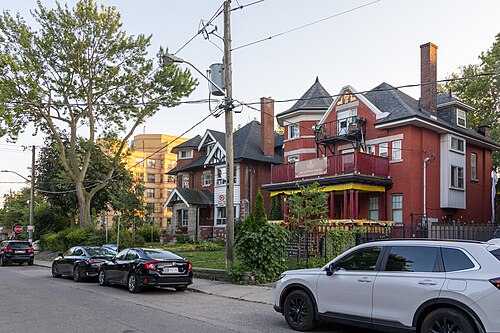 A turreted red brick mansion on Maynard Avenue in use as a Tibetan community space, prayer flags strung across the balcony and a banner in Tibetan script over the entrance.