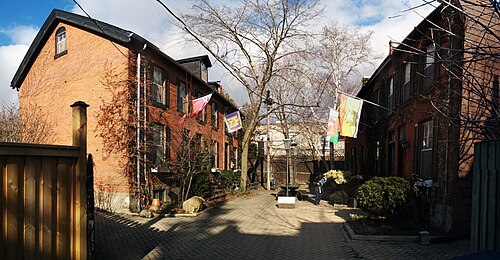 Melbourne Place, a laneway of Victorian row houses in orange brick, prayer flags strung between two of them and a lamppost in the middle of the court.