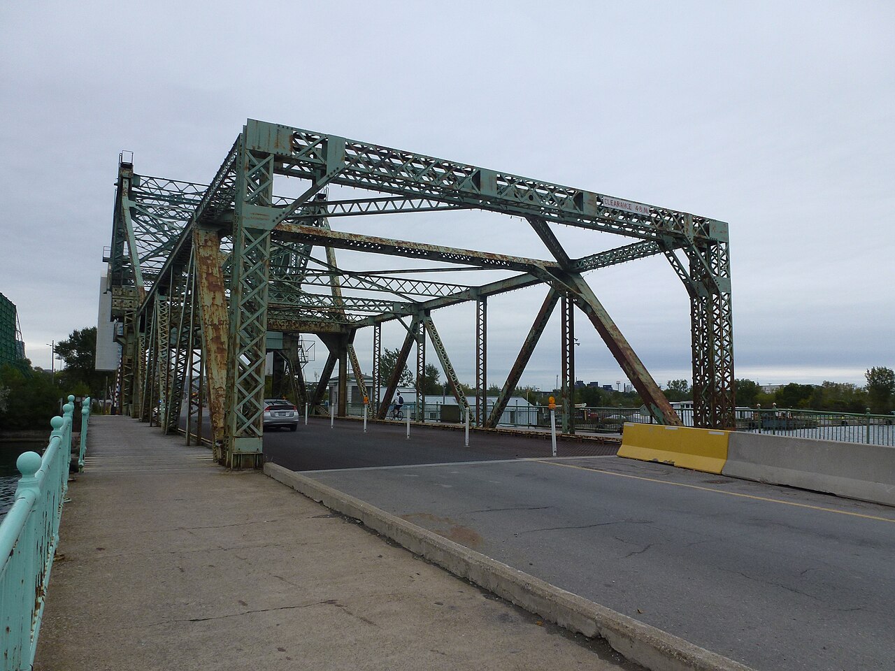 The south end of the Cherry Street bascule bridge, its green steel truss rising over the roadway, a concrete traffic barrier and a cyclist crossing in the foreground.