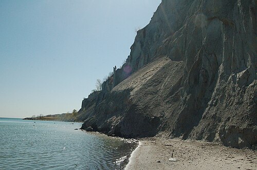 A fan of pale clay debris spread across the beach at the foot of the bluffs where a section of the cliff has slid down, the shoreline receding into the distance.