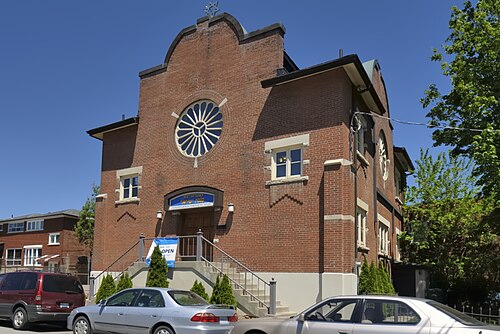 Congregation Knesseth Israel, a red brick synagogue with a round stained glass window and a Star of David at the roofline, cars parked in front.